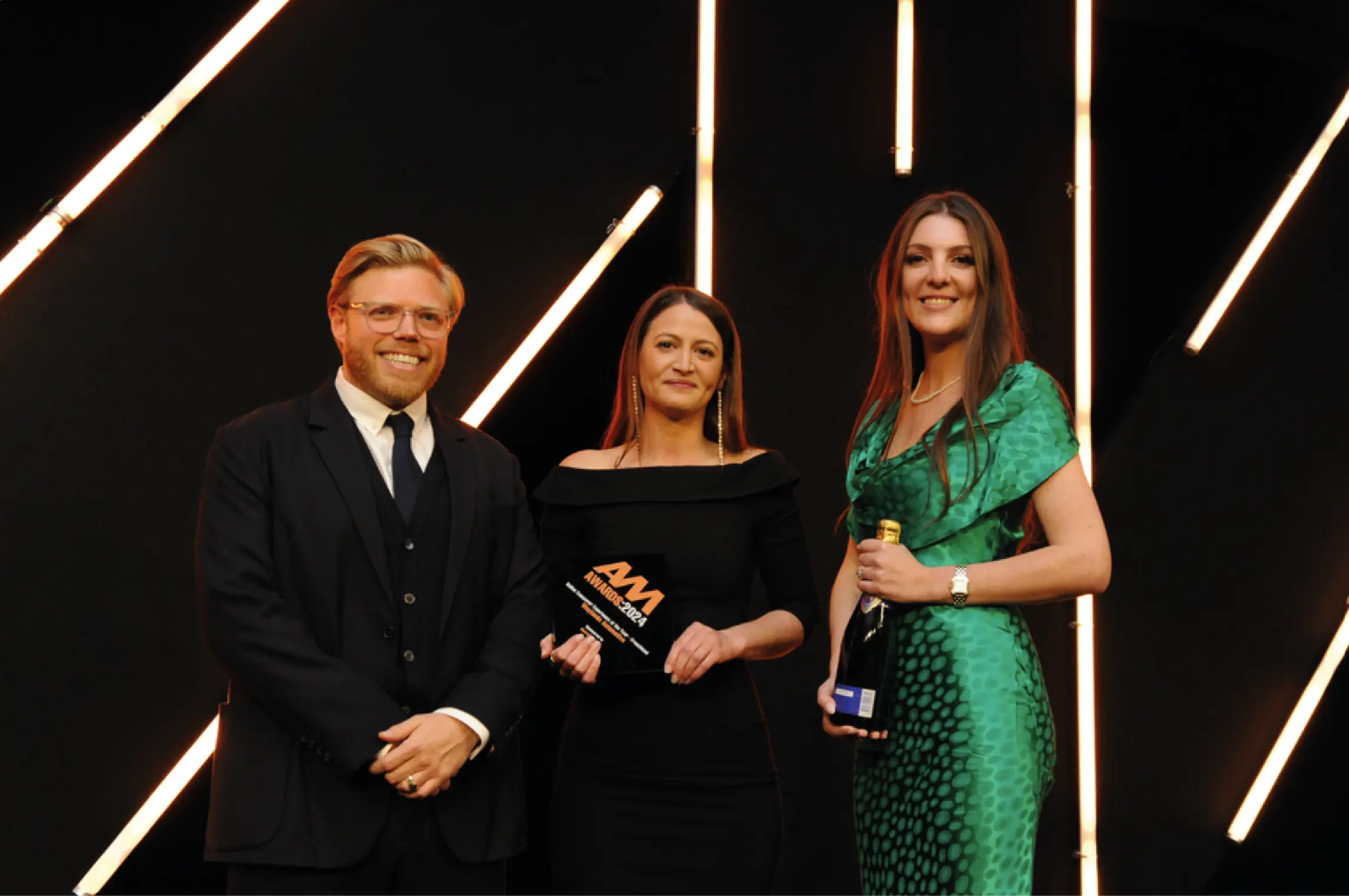A man and two women standing on stage at an award ceremony in front of a black background